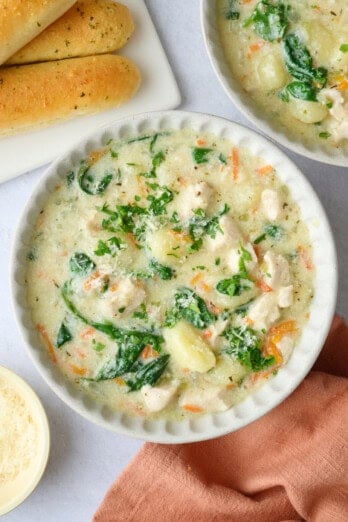Bowl of creamy garlic chicken gnocchi soup garnished with grated parmesan cheese with breadsticks nearby.