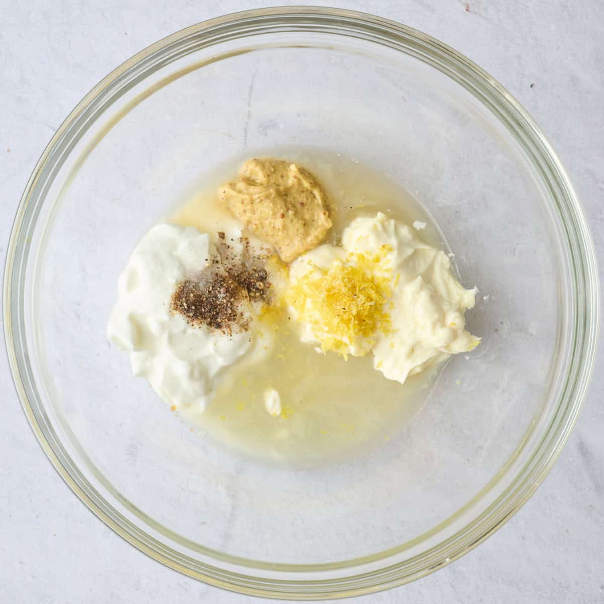 Chickpea liquid, yogurt, mayo, lemon zest and juice, mustard, salt and pepper in a bowl before mixing.