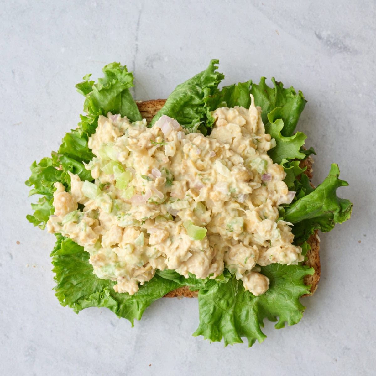 Chickpea salad on top of an open faced sandwich with sliced bread and lettuce.