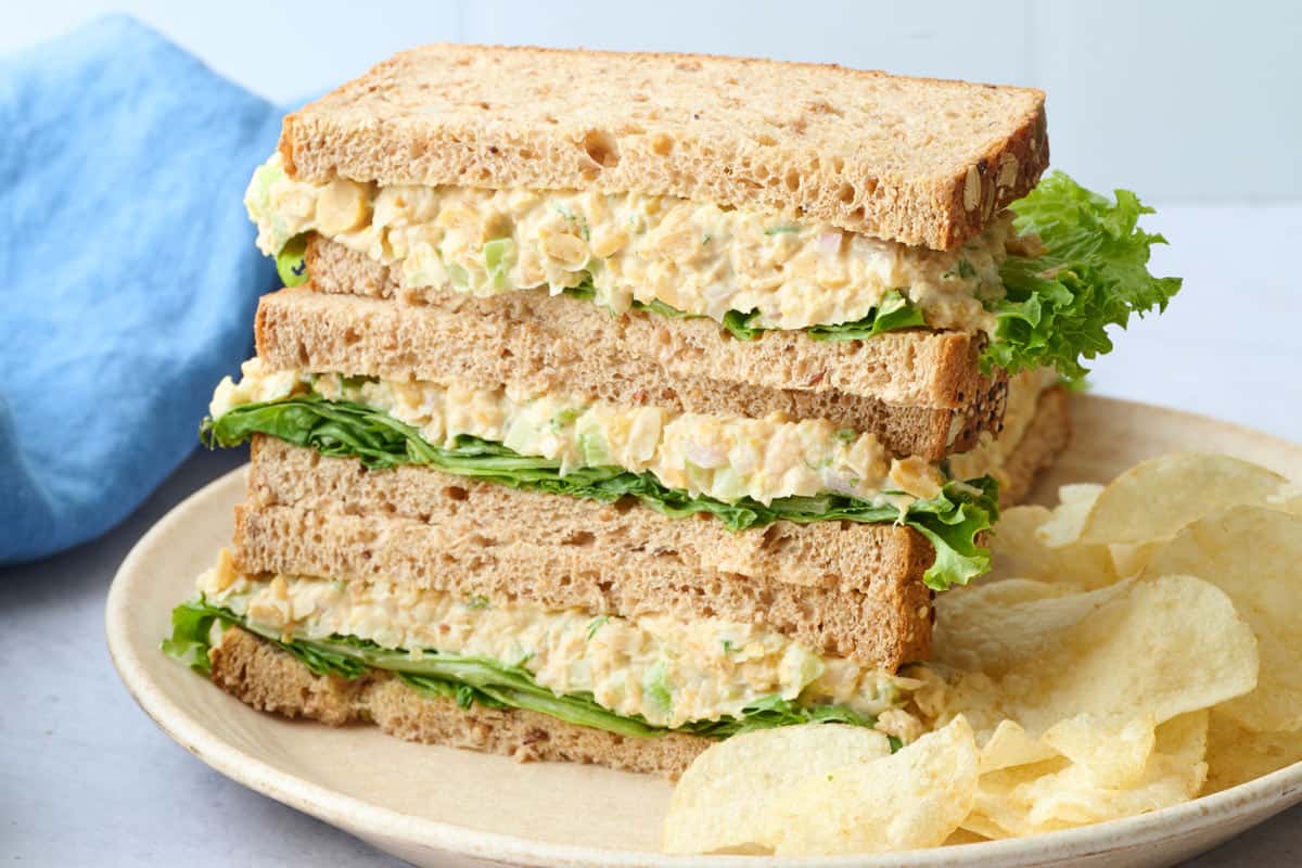 Smashed chickpea salad sandwich cut in half and served on a plate with chips.