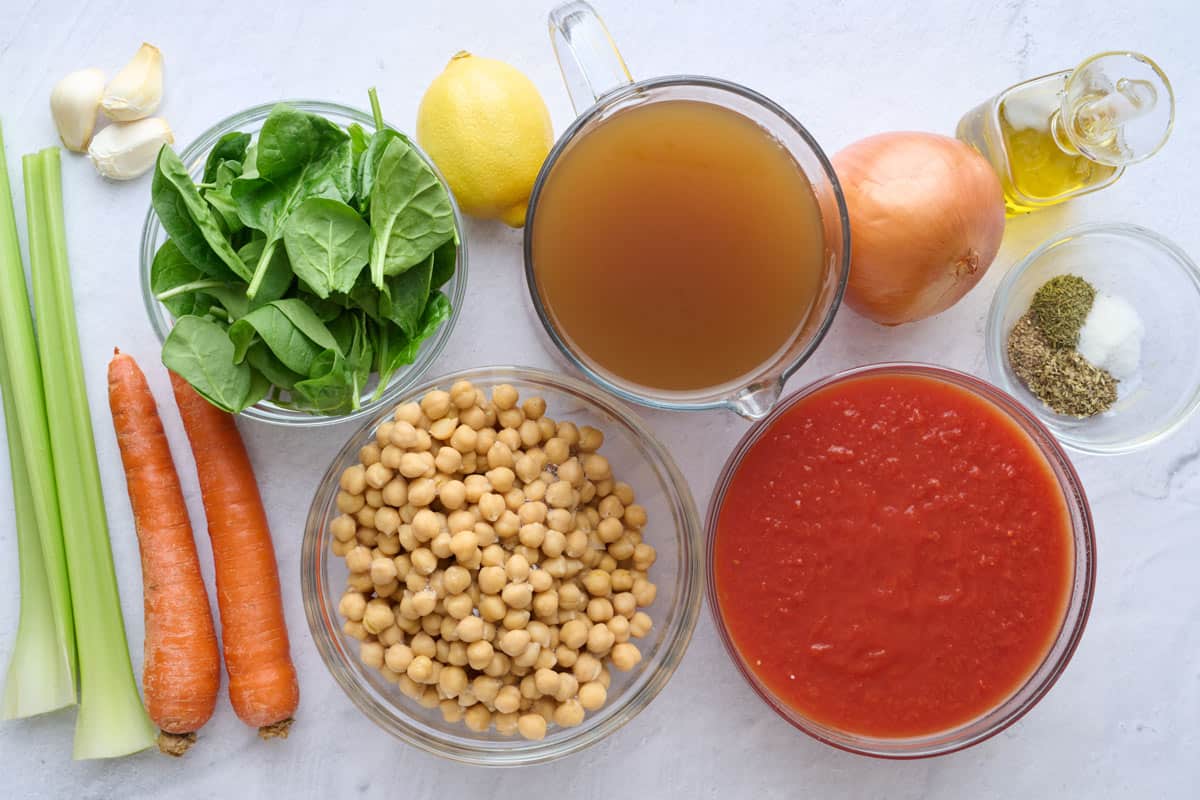 Ingredients for Italian chickpea soup: celery, carrots, spinach, garlic, chickpeas, lemon, broth, crushed tomatoes, seasonings, onion and oil.