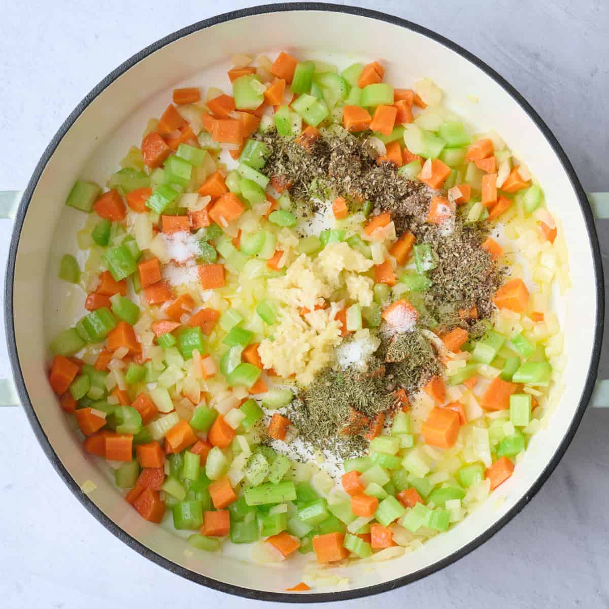 Onion, carrots, celery in a pot after cooking with garlic and seasonings added on top before combining for soup recipe.