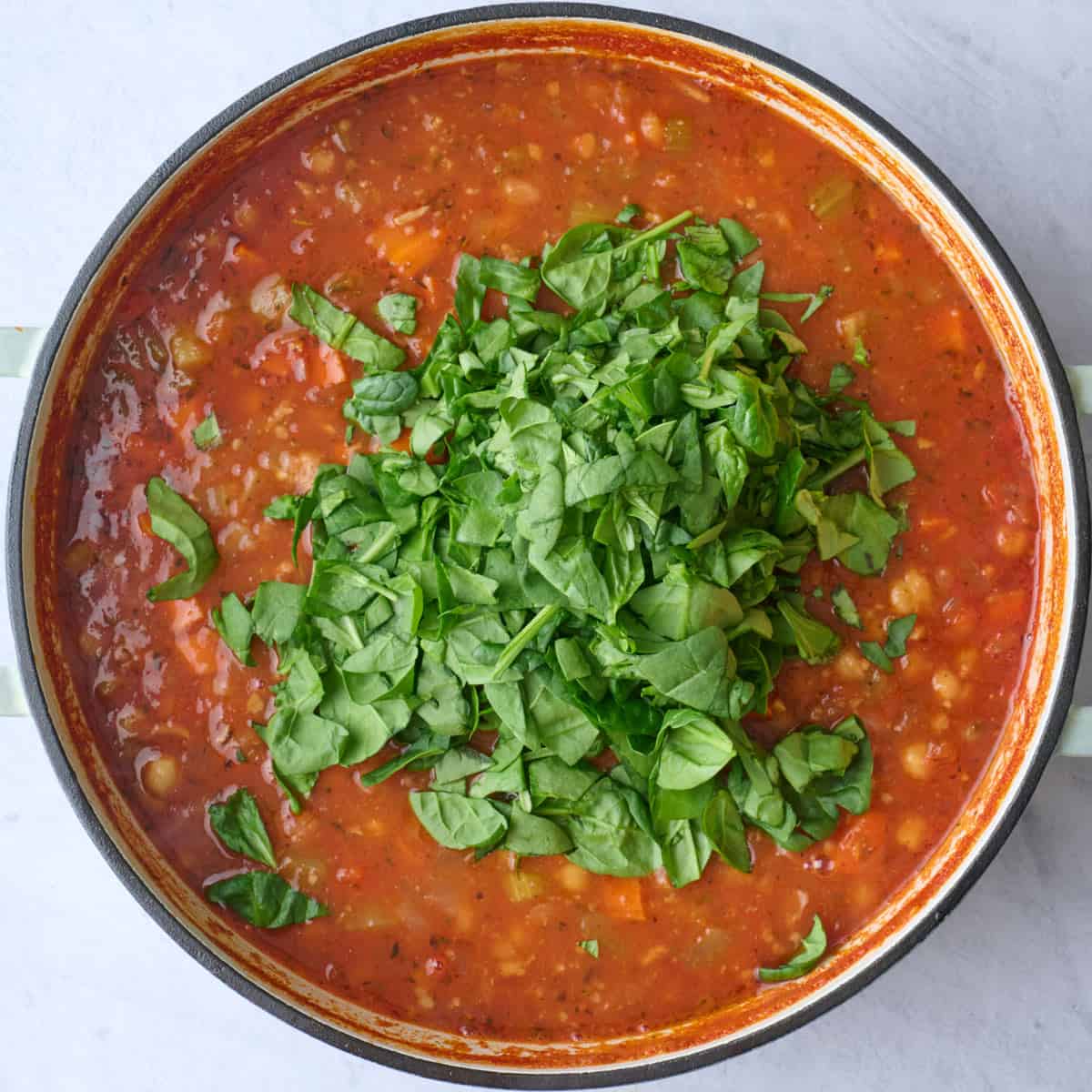 Soup after cooking with spinach added on top before stirring in.