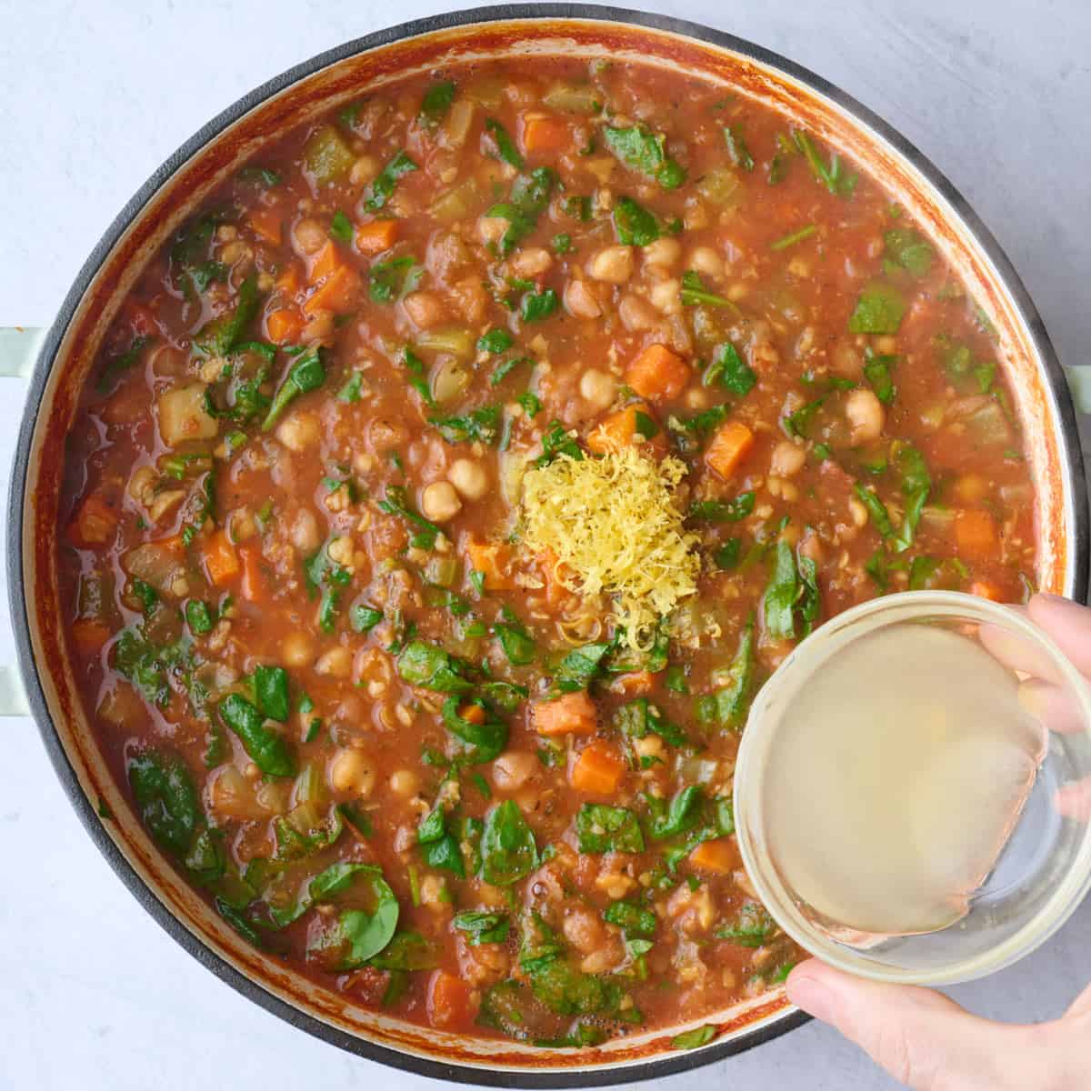 Spinach after combined into chickpea soup with lemon zest added on top and lemon juice being poured in from the side.