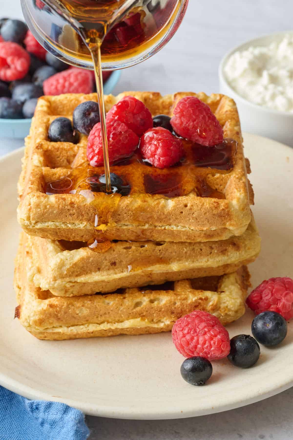 Stack of high protein cottage cheese waffles made with oats on a plate with maple syrup being drizzled on top.