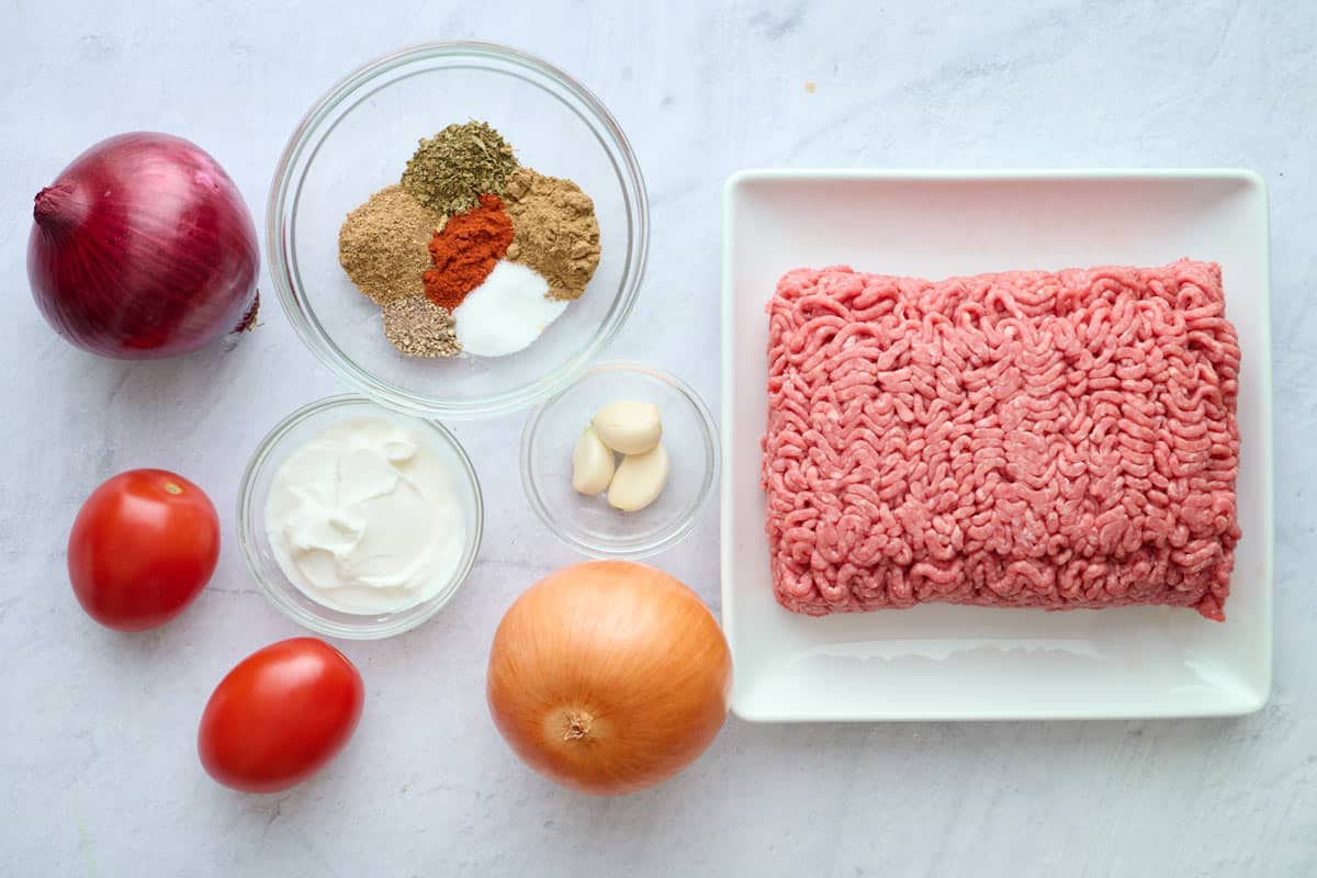 Ingredients for homemade doner kebab recipe: ground beef, onion, garlic, yogurt, spices plus red onion and tomatoes.