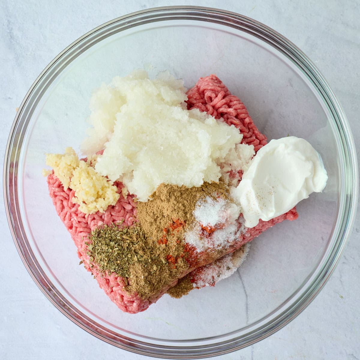 Ground beef, grated onion, garlic, yogurt, cumin, coriander, paprika, oregano, salt, and pepper before mixing.