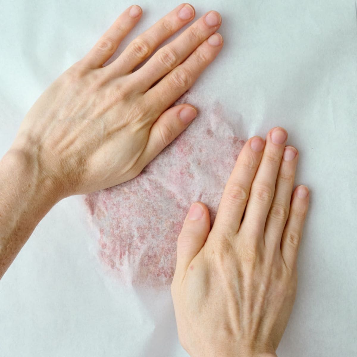 One portion of doner meat on parchment with another parchment on top and hand pressing down on the mixture.