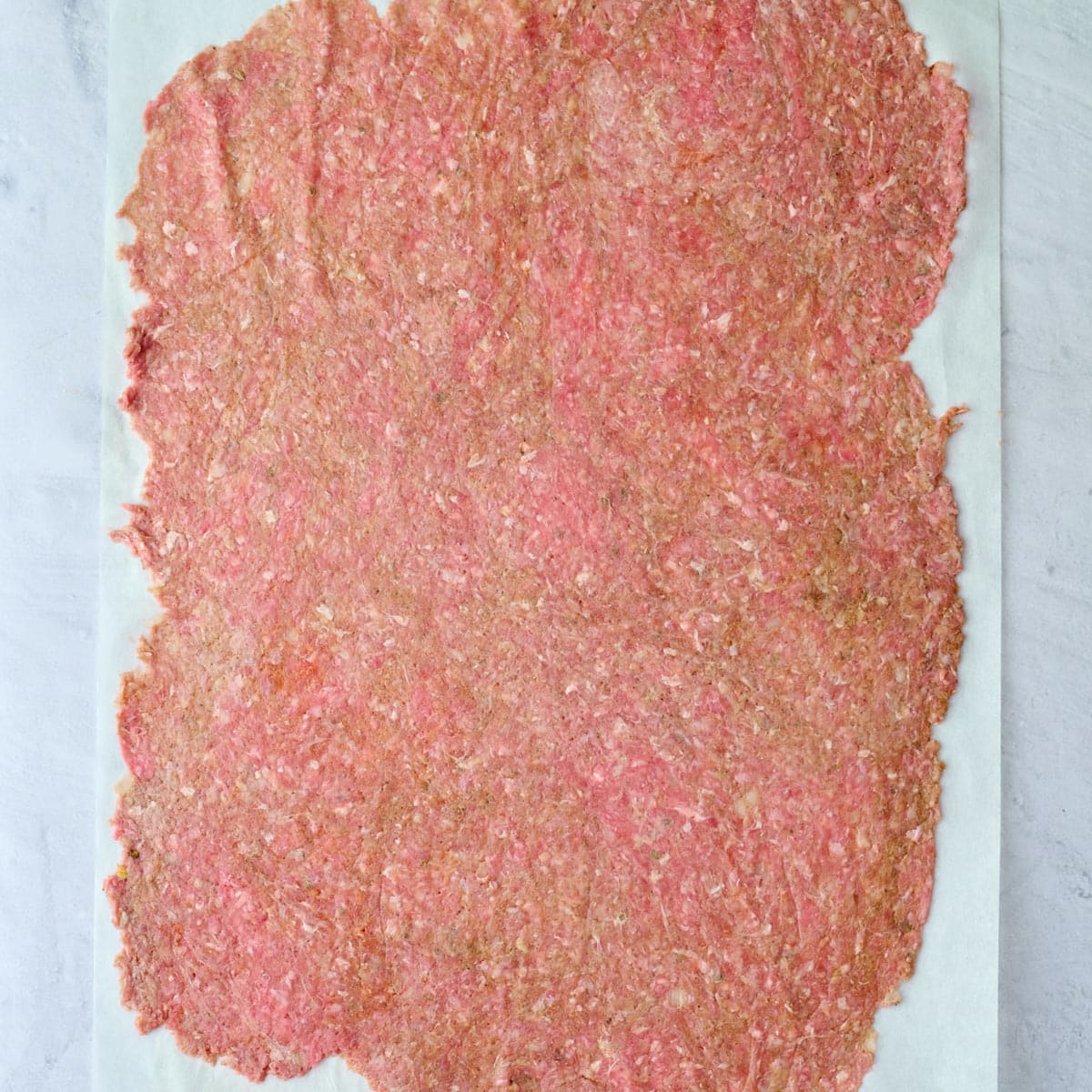 Doner ground beef mixture after shaping into a thin even rectangle on parchment paper.