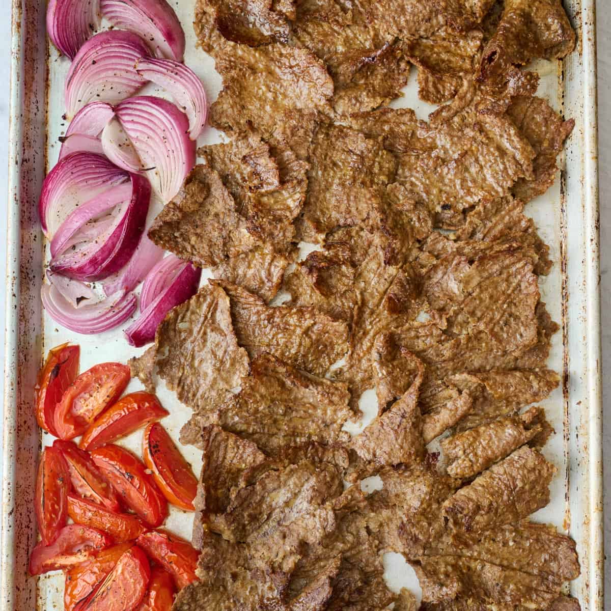 Broiled doner kebab meat on a sheet pan with onions and tomatoes.