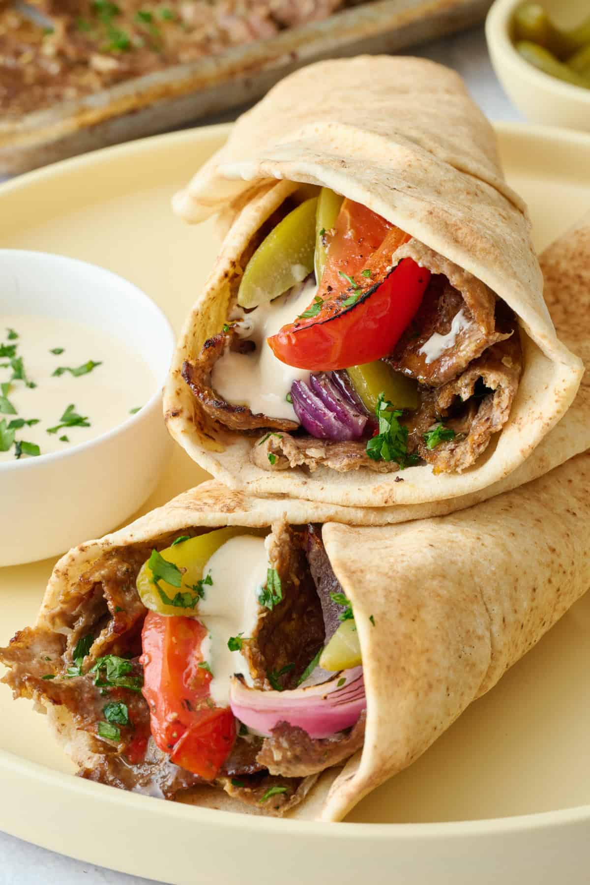 Doner kebab stuffed pita with tomatoes, onions and tahini sauce on a plate.
