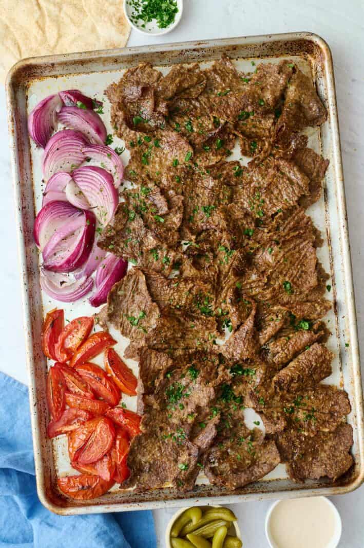 Homemade doner kebab recipe on a sheet pan with roasted tomatoes and onions.