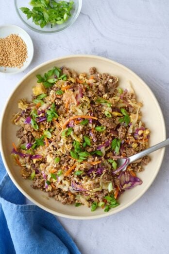 Egg roll filling with coleslaw mix served in a bowl, garnished with green onions and sesame seeds.