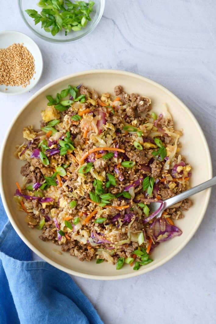 Egg roll filling with coleslaw mix served in a bowl, garnished with green onions and sesame seeds.