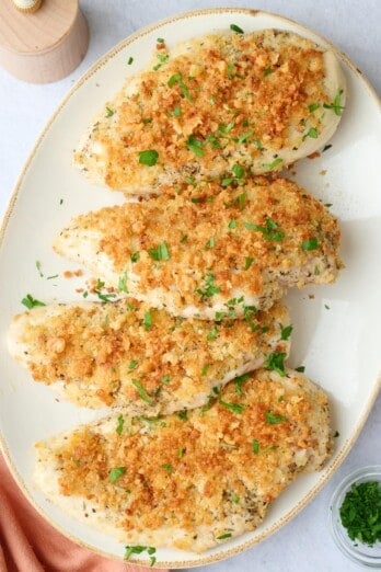 Best garlic parmesan chicken recipe on a platter garnished with chopped parsley.