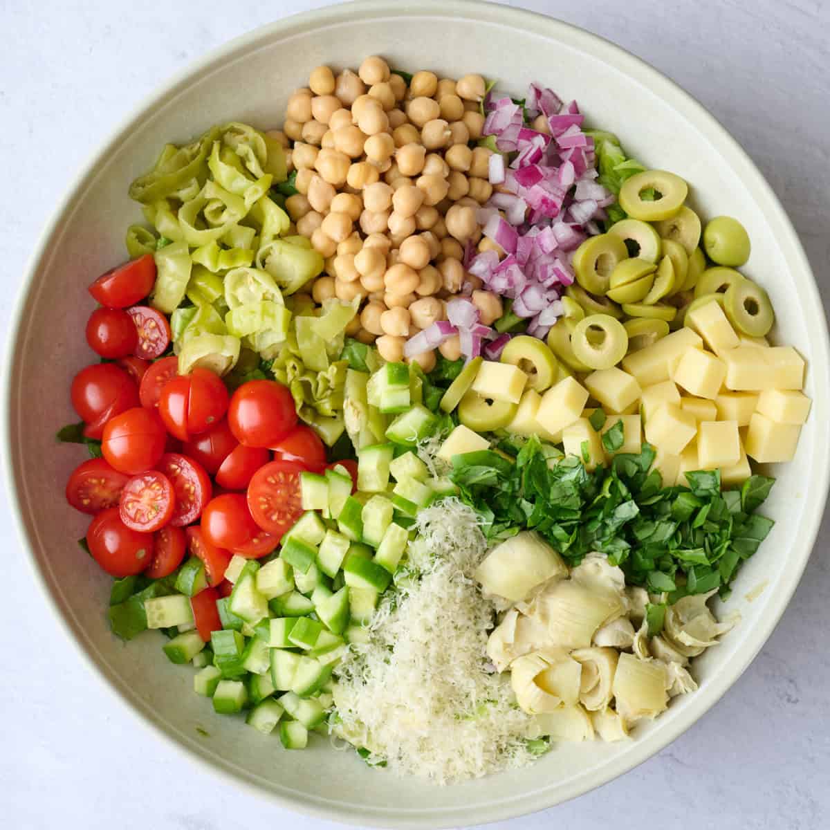 Salad ingredients added in segments on top of chopped lettuce before being tossed together.