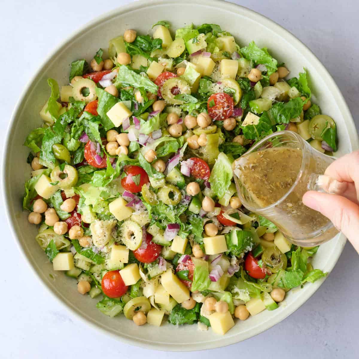 Homemade Italian dressing being poured over chopped salad.