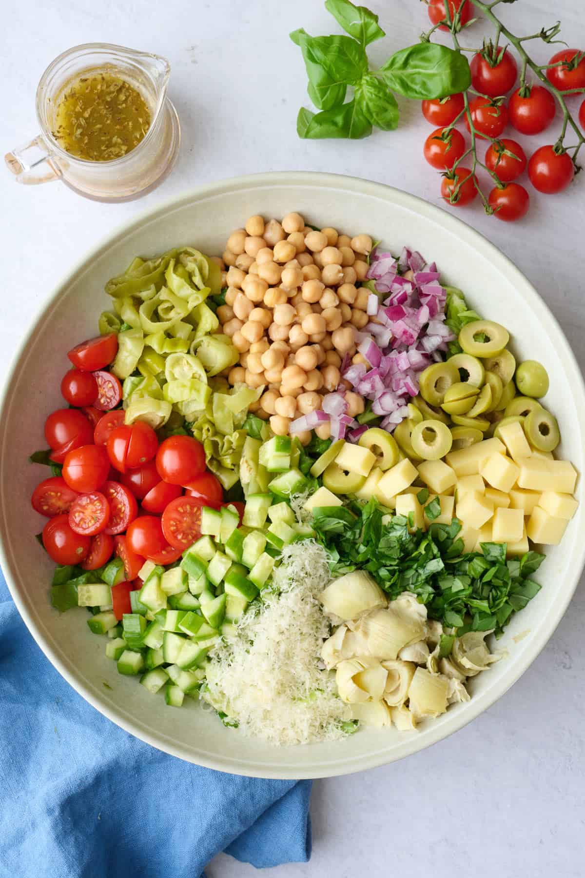 Italian chopped salad ingredients in a serving bowl before tossing together with a homemade dressing nearby.