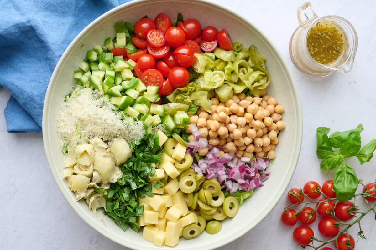 Italian chopped salad ingredients in a serving bowl before tossing together with a homemade dressing nearby.