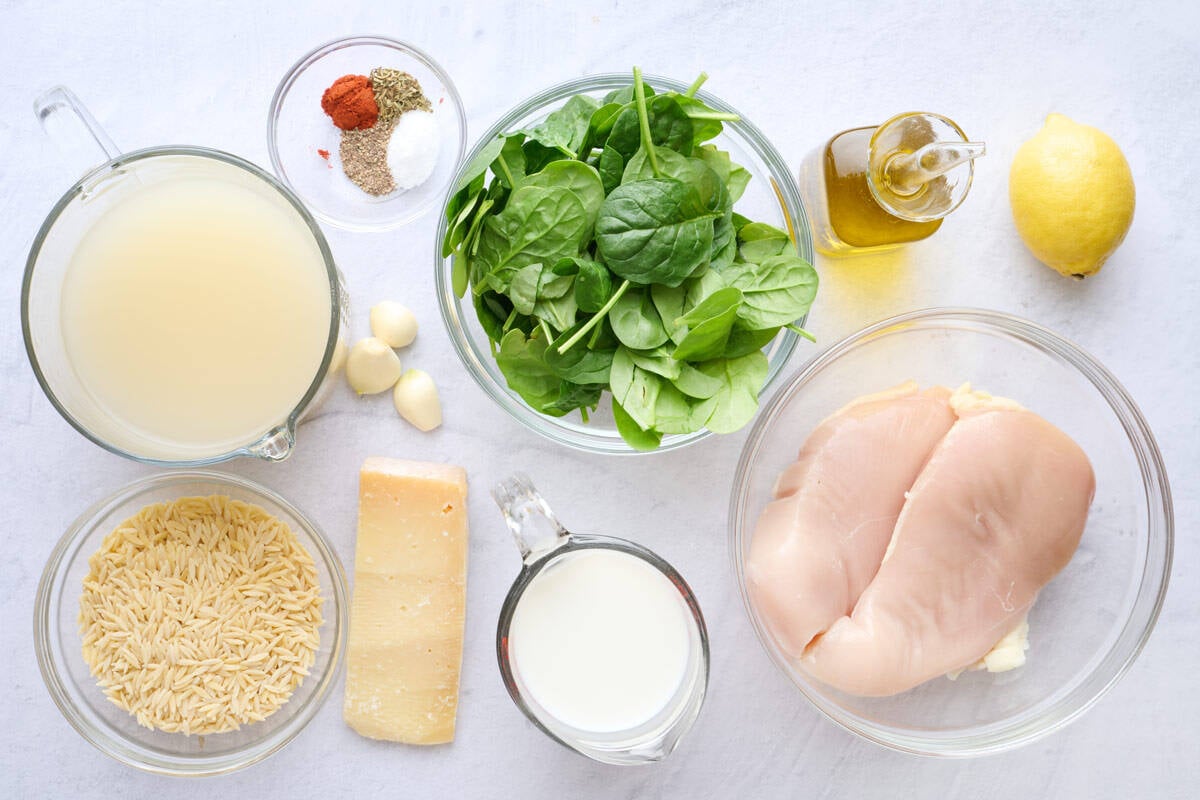 Ingredients for one pan recipe: broth, seasonings, orzo, parmesan cheese, garlic cloves, fresh spinach, milk, oil, chicken breasts and lemon.