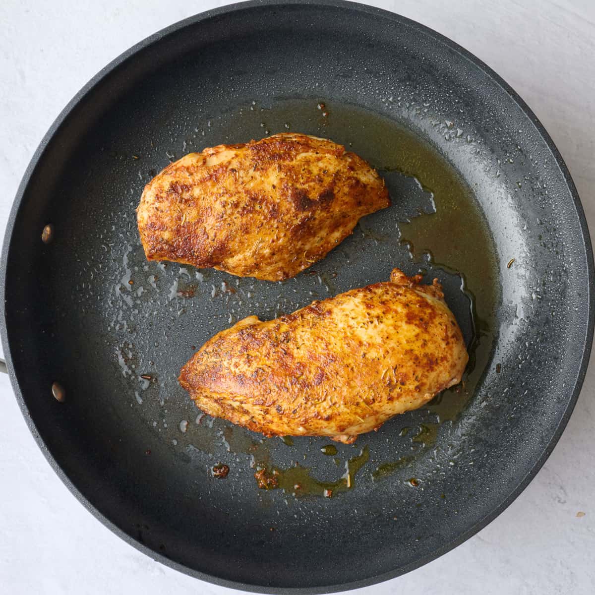 Seasoned cooked chicken breast in a pan.