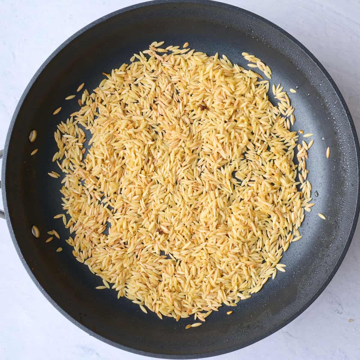 Garlic after sautéing in chicken drippings with orzo added and toasted.