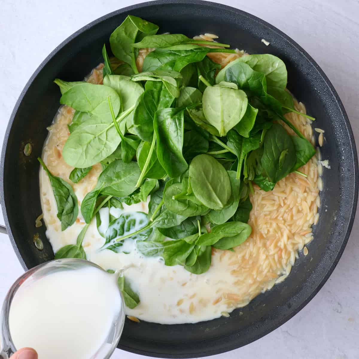 Spinach added to cooked orzo with milk being added in before combining.