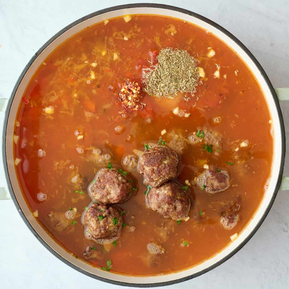 Crushed tomatoes, broth, and seasonings and cooked meatballs added before combining.