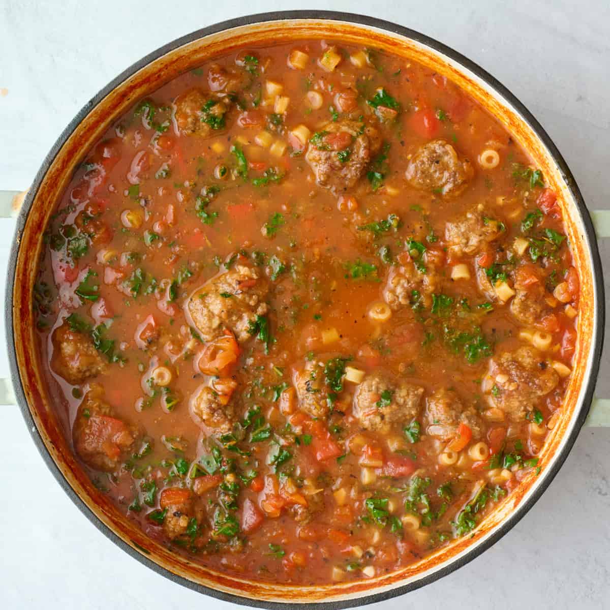 Final meatball soup recipe in the pot with small pasta and kale.