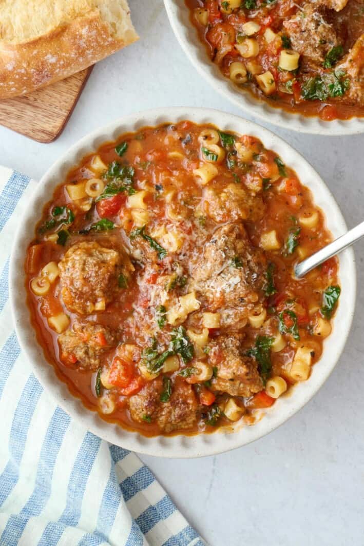 Two bowls of Italian meatball soup, garnished with parmesan cheese.