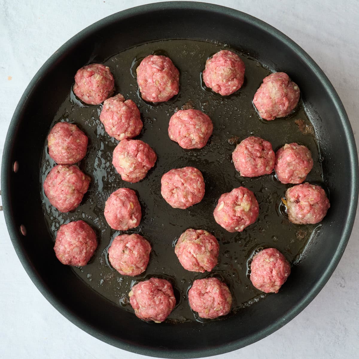Ground beef meatballs in an oiled skillet.