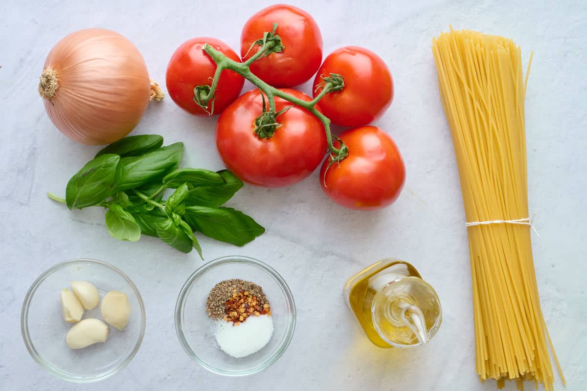 Ingredients for recipes: onion, tomatoes, fresh basil, garlic cloves, salt, pepper and red pepper flakes, oil, and spaghetti pasta.