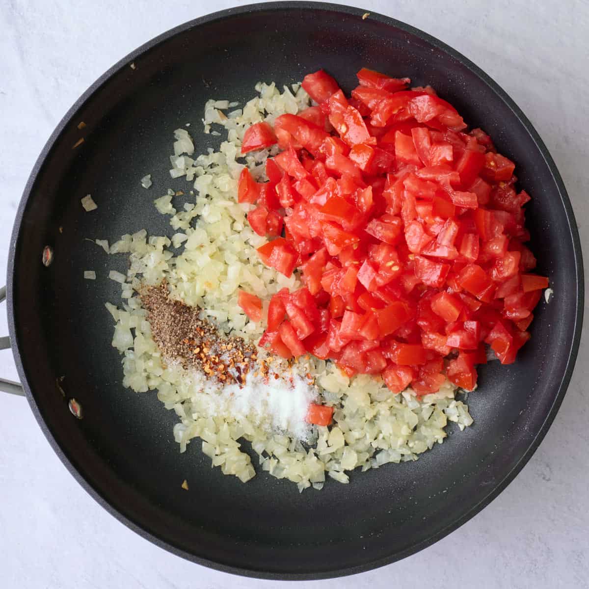 Onions and garlic after cooking in a large skillet with diced tomatoes, salt, pepper and red pepper flakes added before combining.