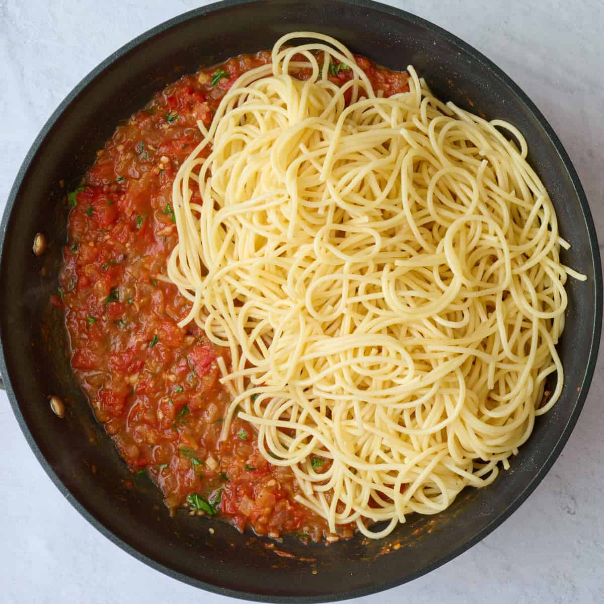 Cooked pasta added on top of pomodoro sauce before tossing together.