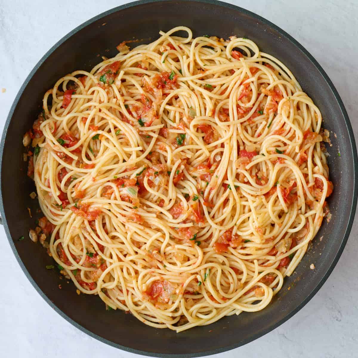 Pasta tossed in tomato sauce in a pan.