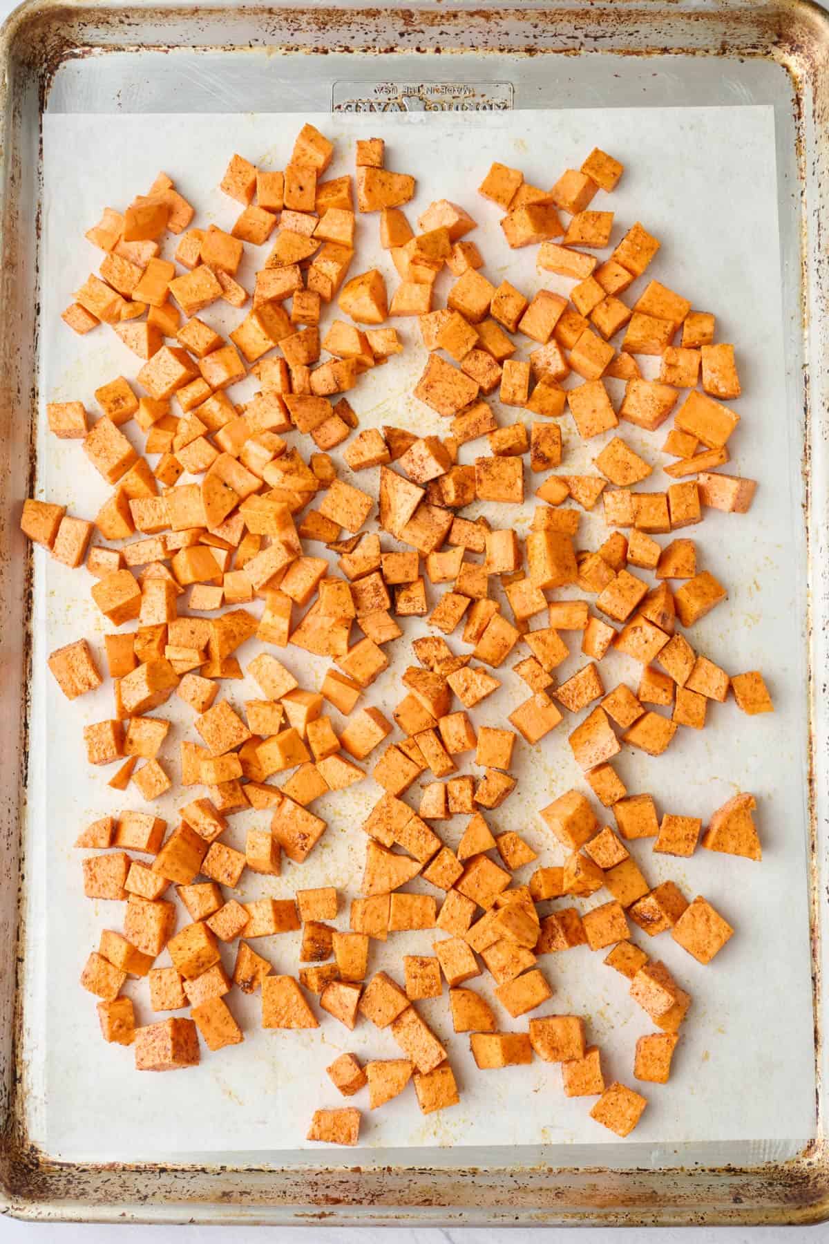 Spiced sweet potato cubes on a sheet pan before roasted.