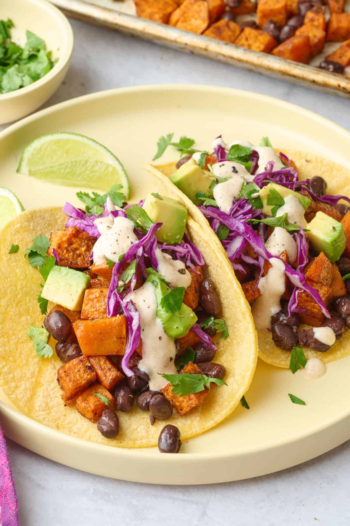 Two assembled sweet potato tacos with shredded red cabbage and creamy sauce.