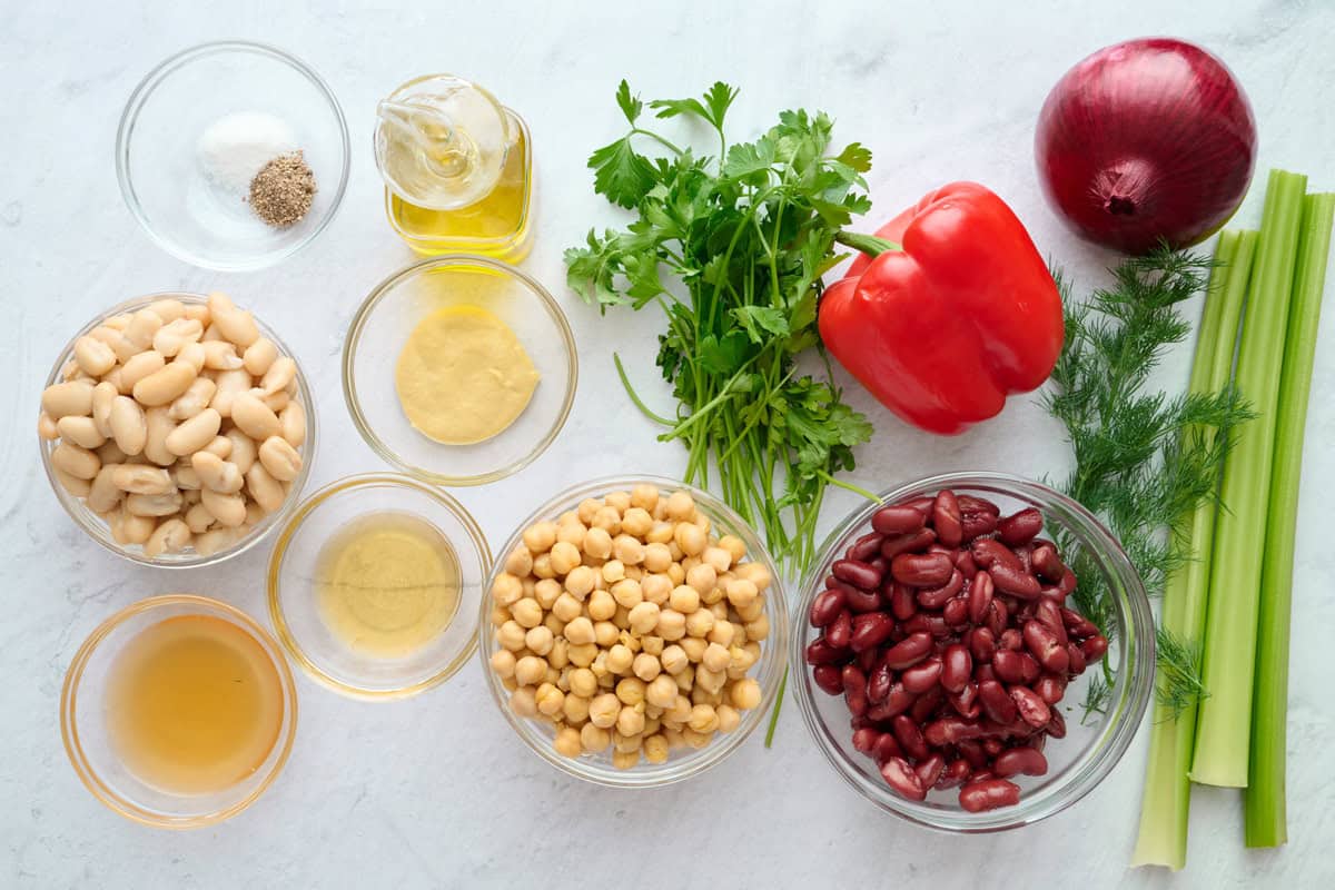 Ingredients for salad recipe: cannellini beans, kidney beans, chickpeas, red pepper, red onion, parsley, dill, celery, apple cider vinegar, dijon mustard, honey, salt, pepper, and oil.