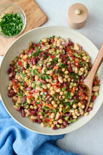 Easy three bean salad in a serving dish with spoon dipped inside garnished with extra chopped parsley.