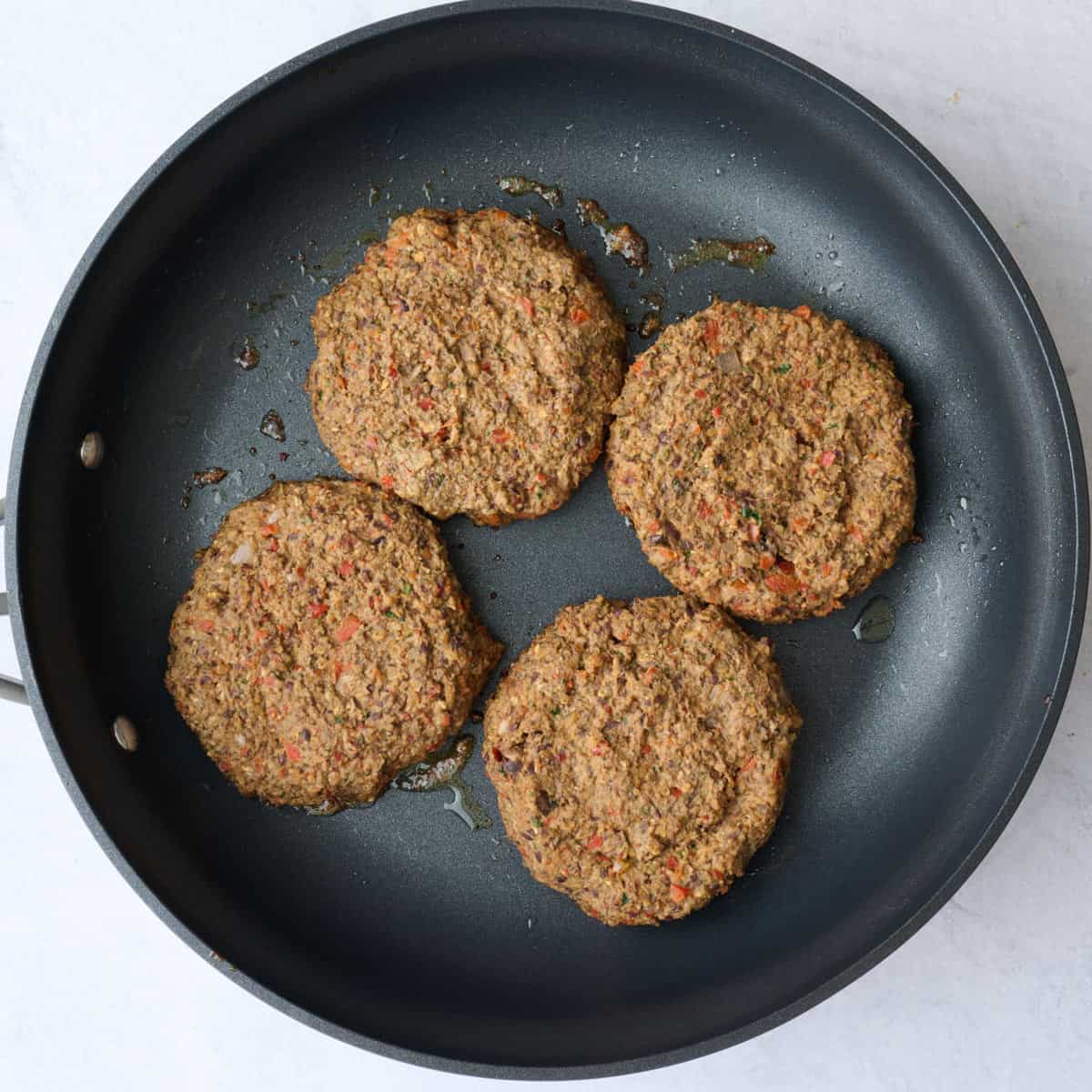 Four veggie burger patties in an oiled non stick skillet before cooking.