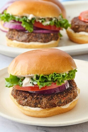 Thick and hearty veggie burger patty served on a bun with toppings and more assembled burgers nearby.