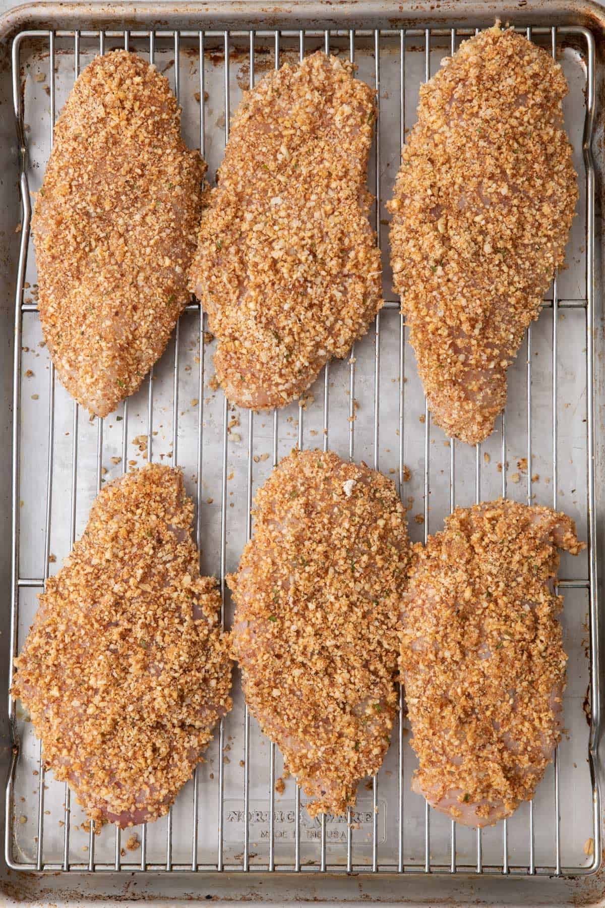 Almond coated chicken breast cutlets on a wire rack on top of a baking sheet before baking.