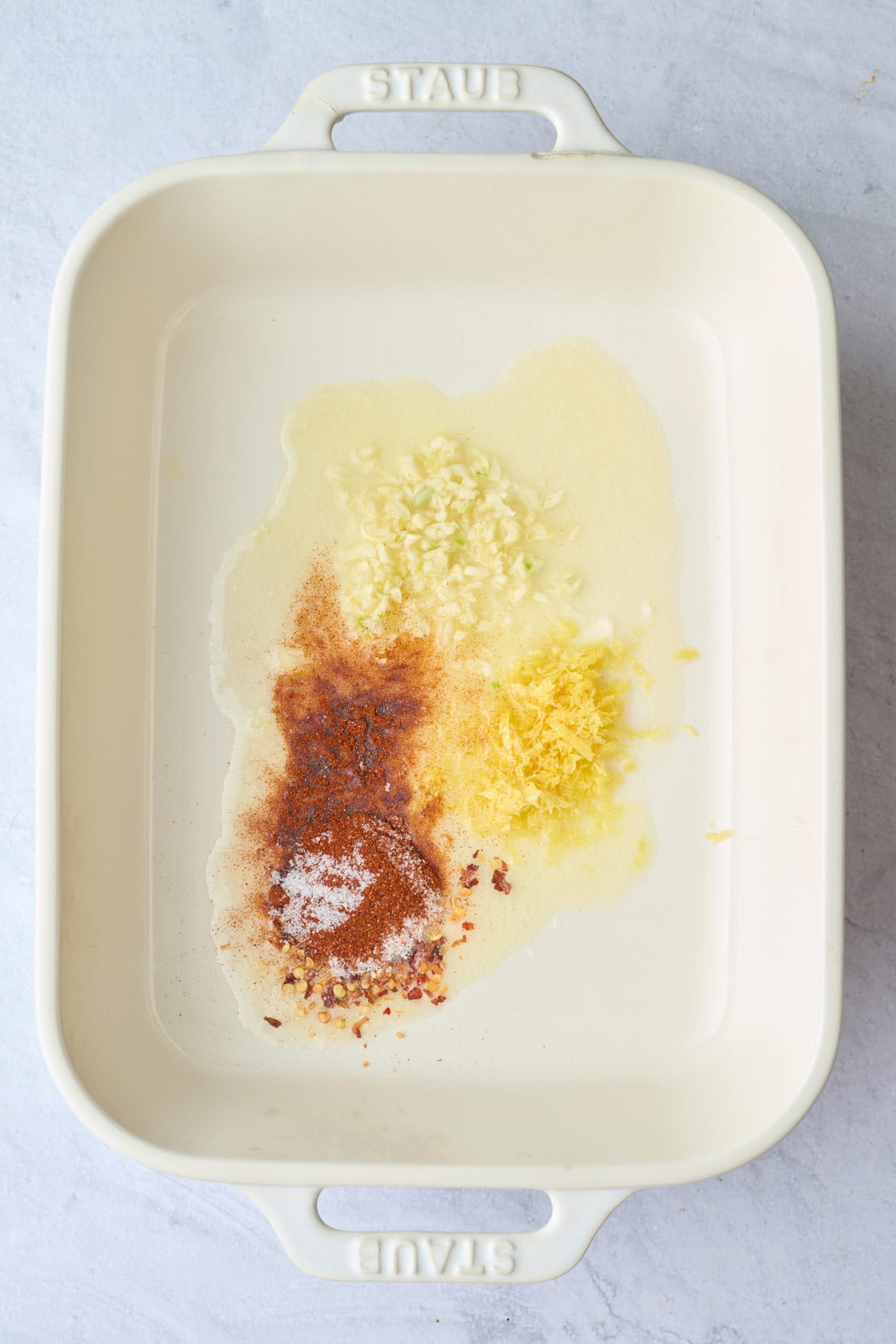 Melted butter in a baking dish with garlic, salt, paprika, red pepper flakes, and lemon zest added before whisking.