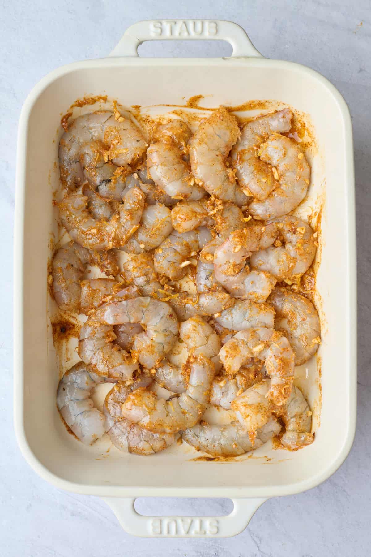 Shrimp tossed in seasoning in a baking dish before cooking.