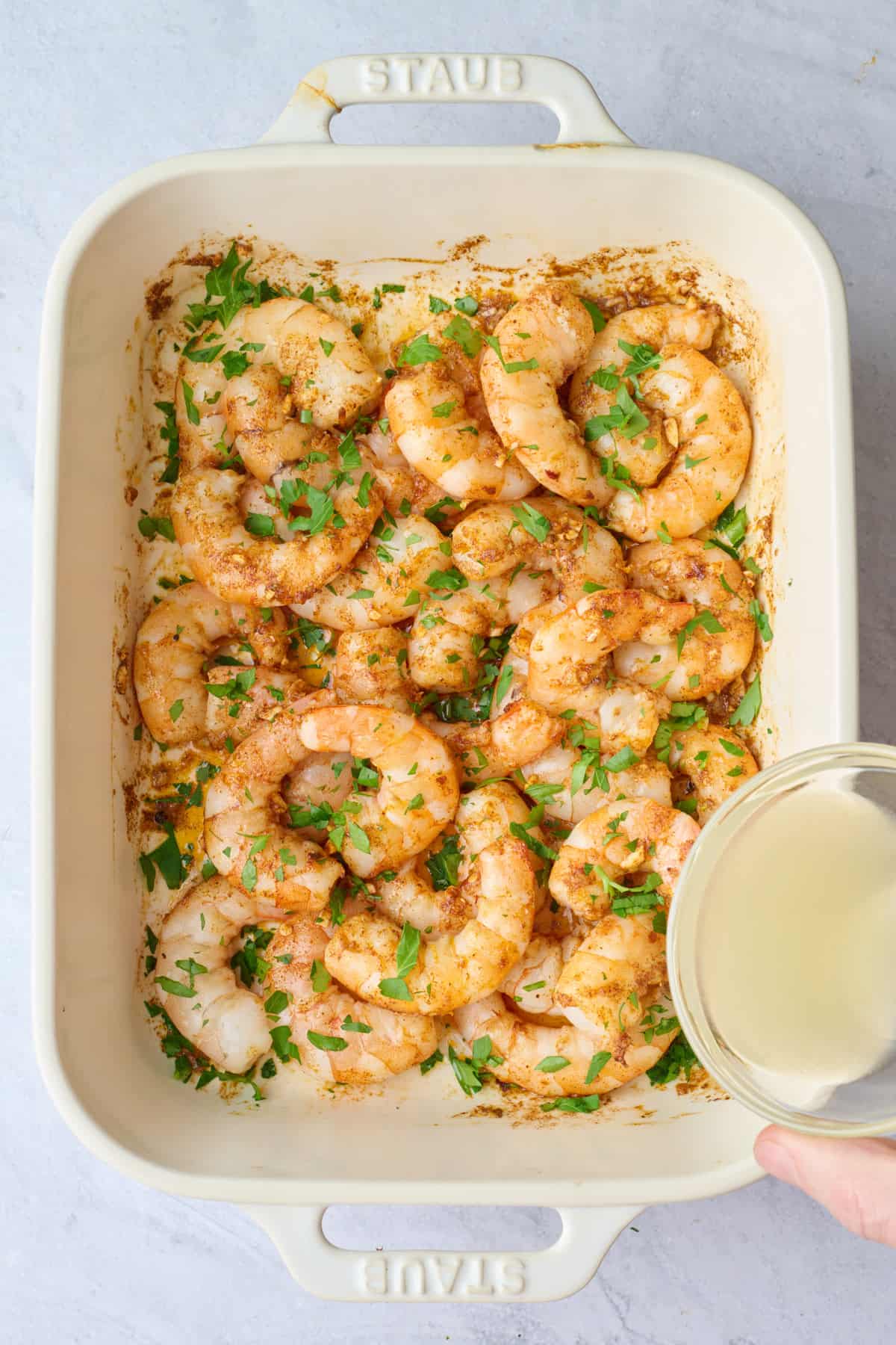Parsley added on top of baked shrimp with lemon juice being poured in.