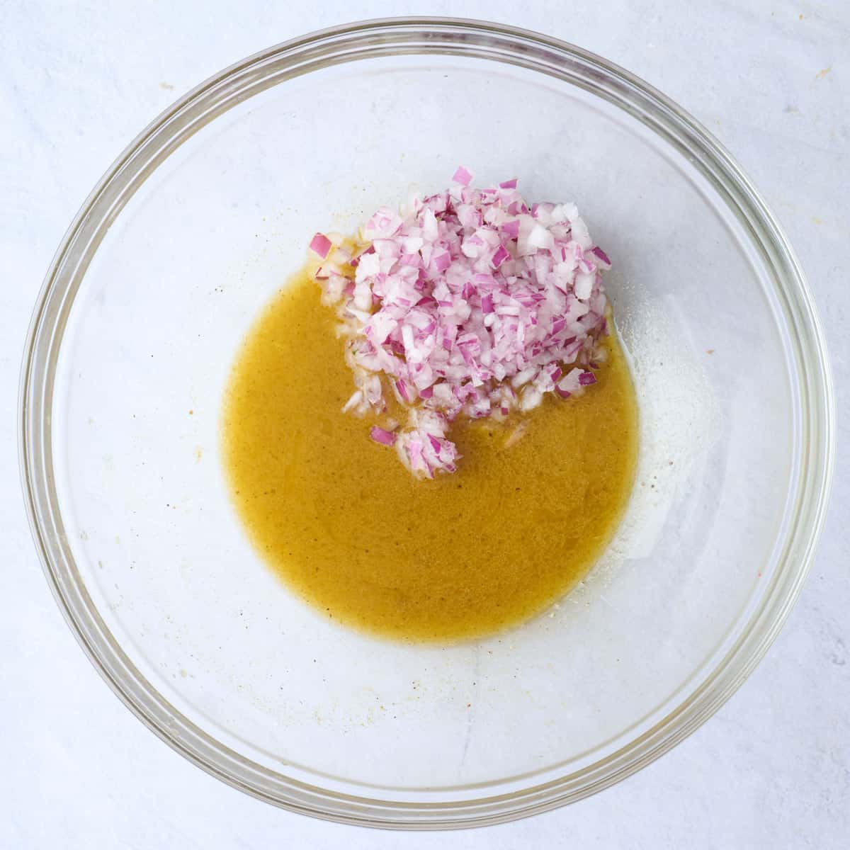 Lemon juice, oil, and seasonings in a bowl after whisking with red onions added on top.