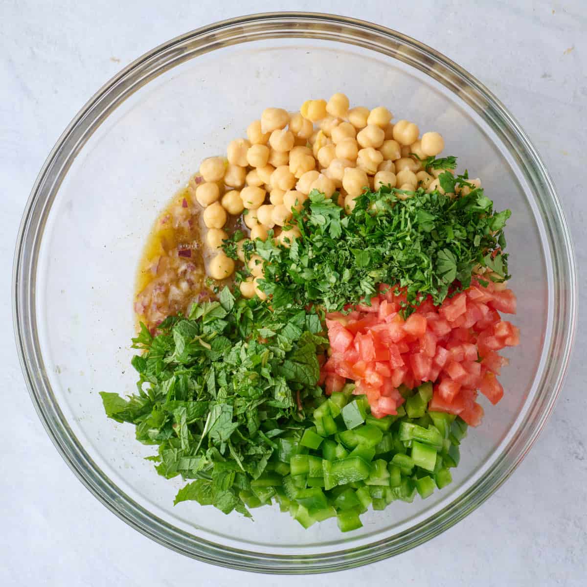 Chickpeas, tomatoes, bell pepper, parsley and mint added on top with red onion dressing still visible.