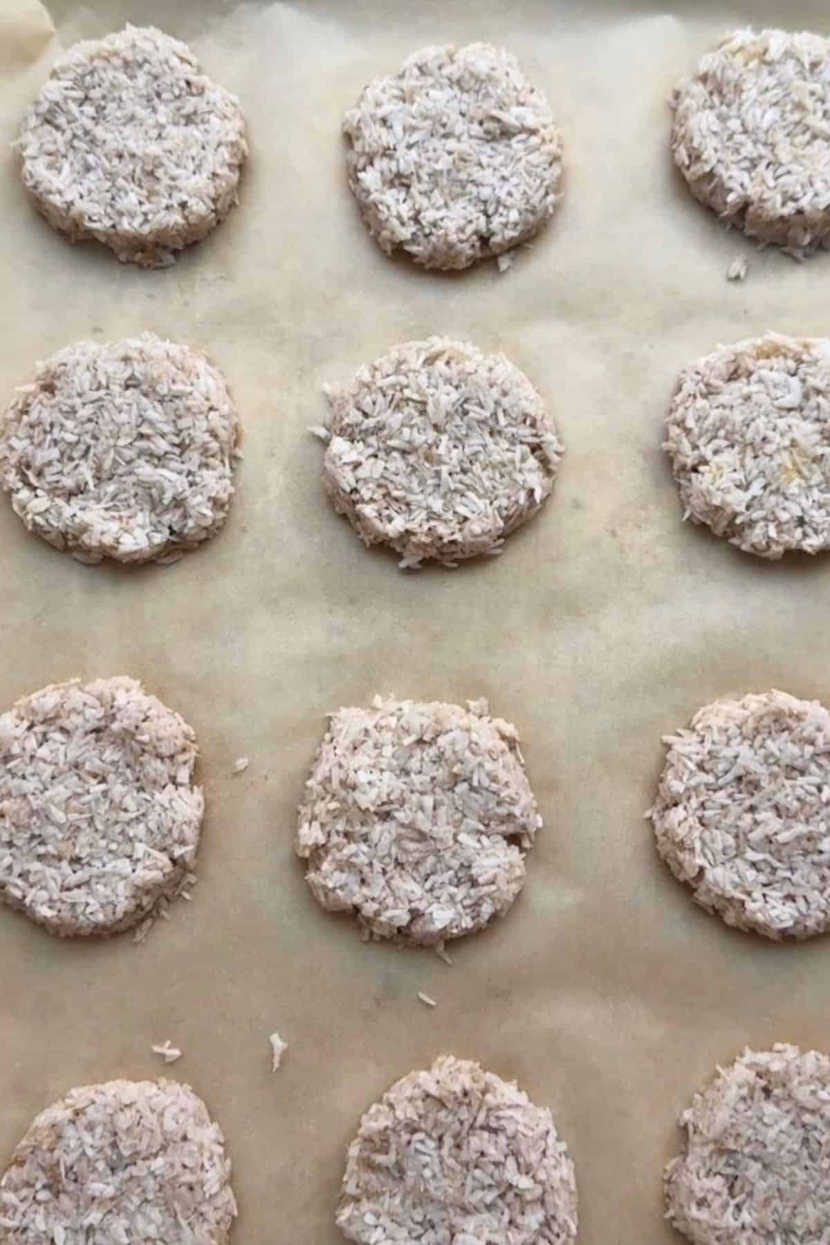 Coconut cookies flattened into rounds on a baking sheet before baking.