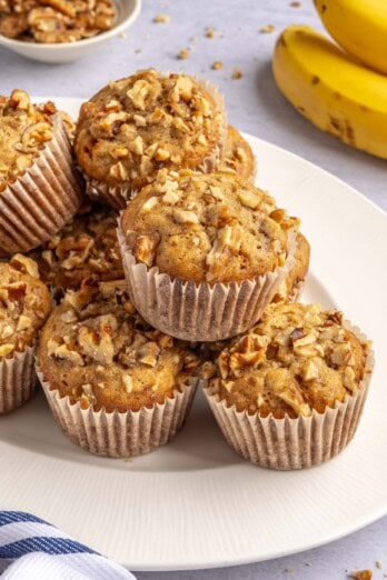 Easy banana nut muffins piled on a platter with walnuts and whole bananas nearby.