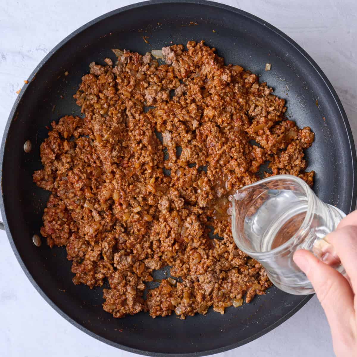 Water being added to seasoned ground beef in pan.